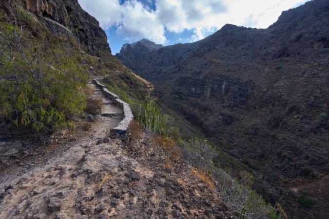 A narrow stone-edged mountain trail winding along a steep cliff, perfect for a first trek in a dramatic canyon landscape.