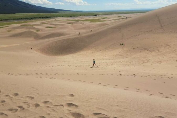 A hiker walking down a massive slope while exploring remote sand dunes.