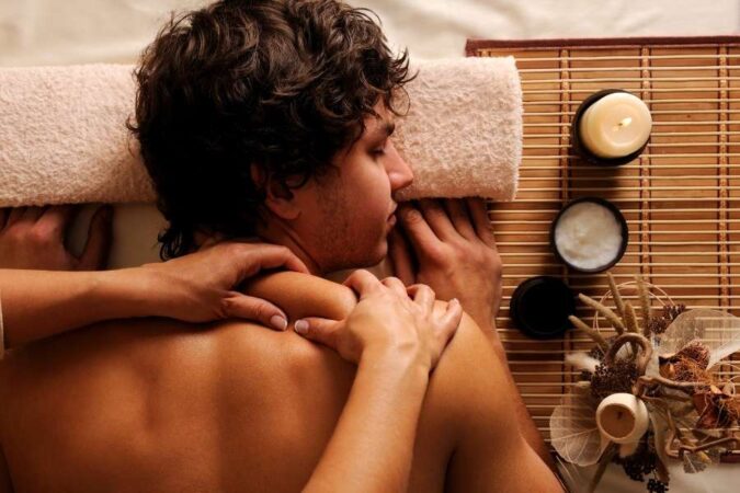 A man lying face down on a massage table while a therapist massages his shoulders.