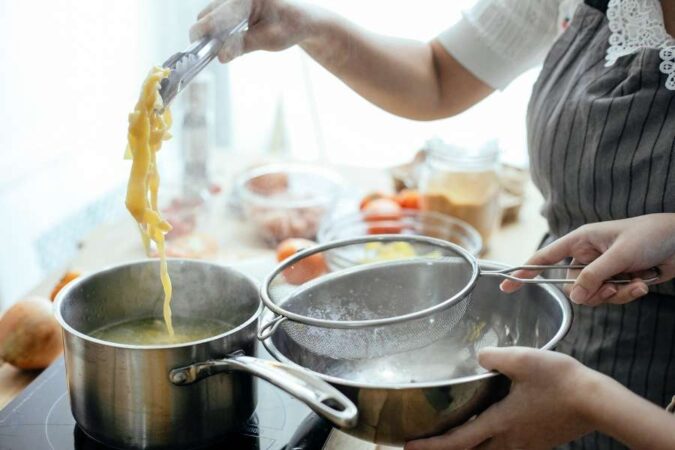 A cook using tongs to check noodles while preparing easy one-pot recipes to cook.