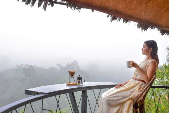 A woman in a light dress sits on a balcony overlooking a misty jungle for a relaxing Khao Sok with kids trip